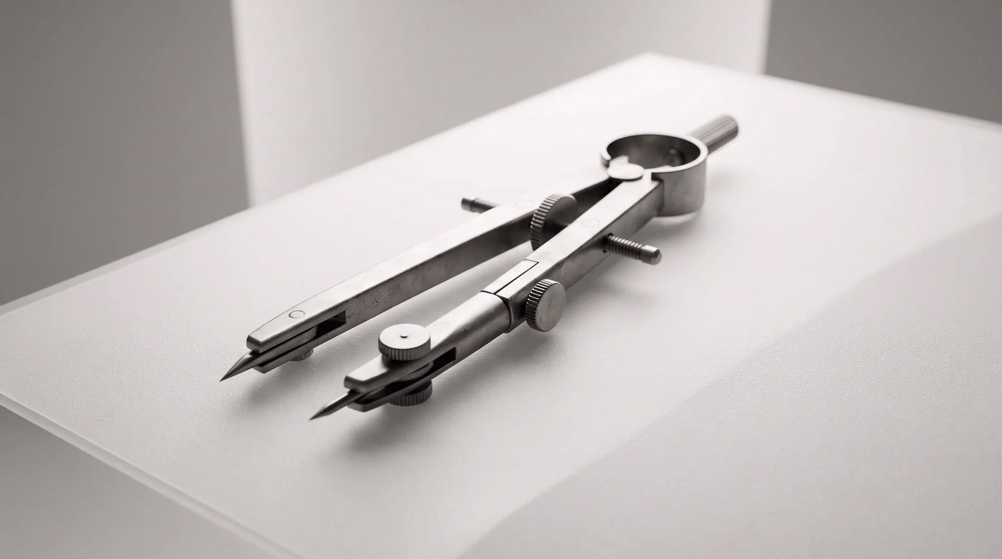 A metal drafting compass rests on a smooth white surface.
